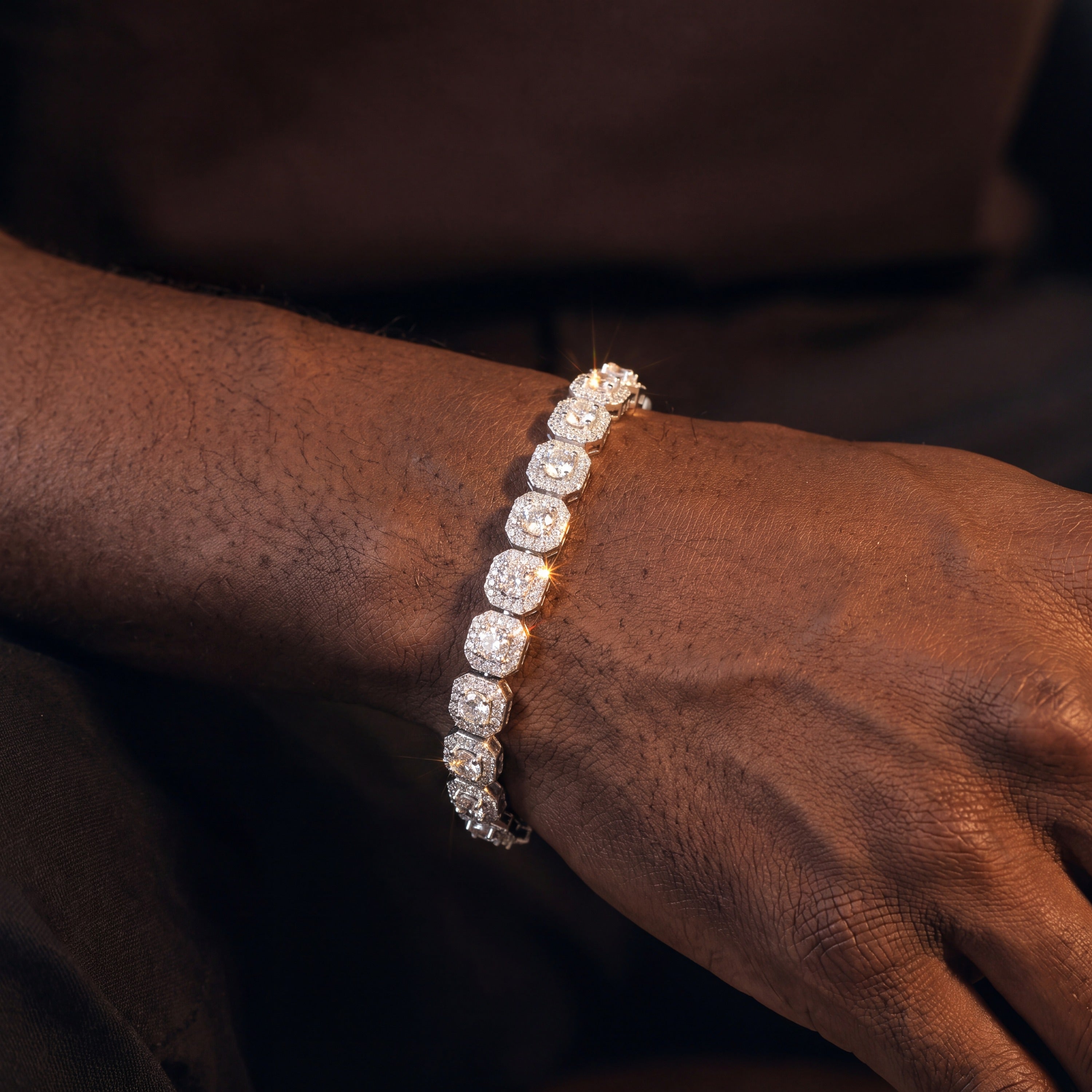 Iced cluster tennis bracelet worn resting on a dark seat